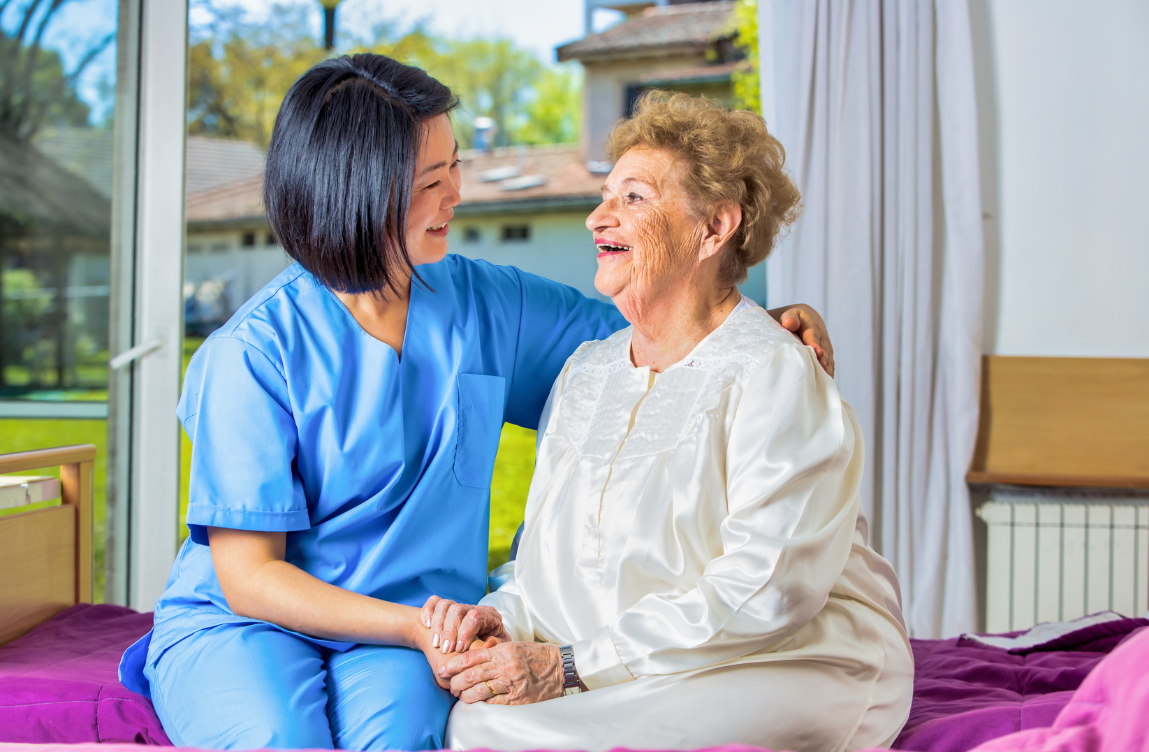 Home health care. Asian nurse consoling elderly lady just woken up